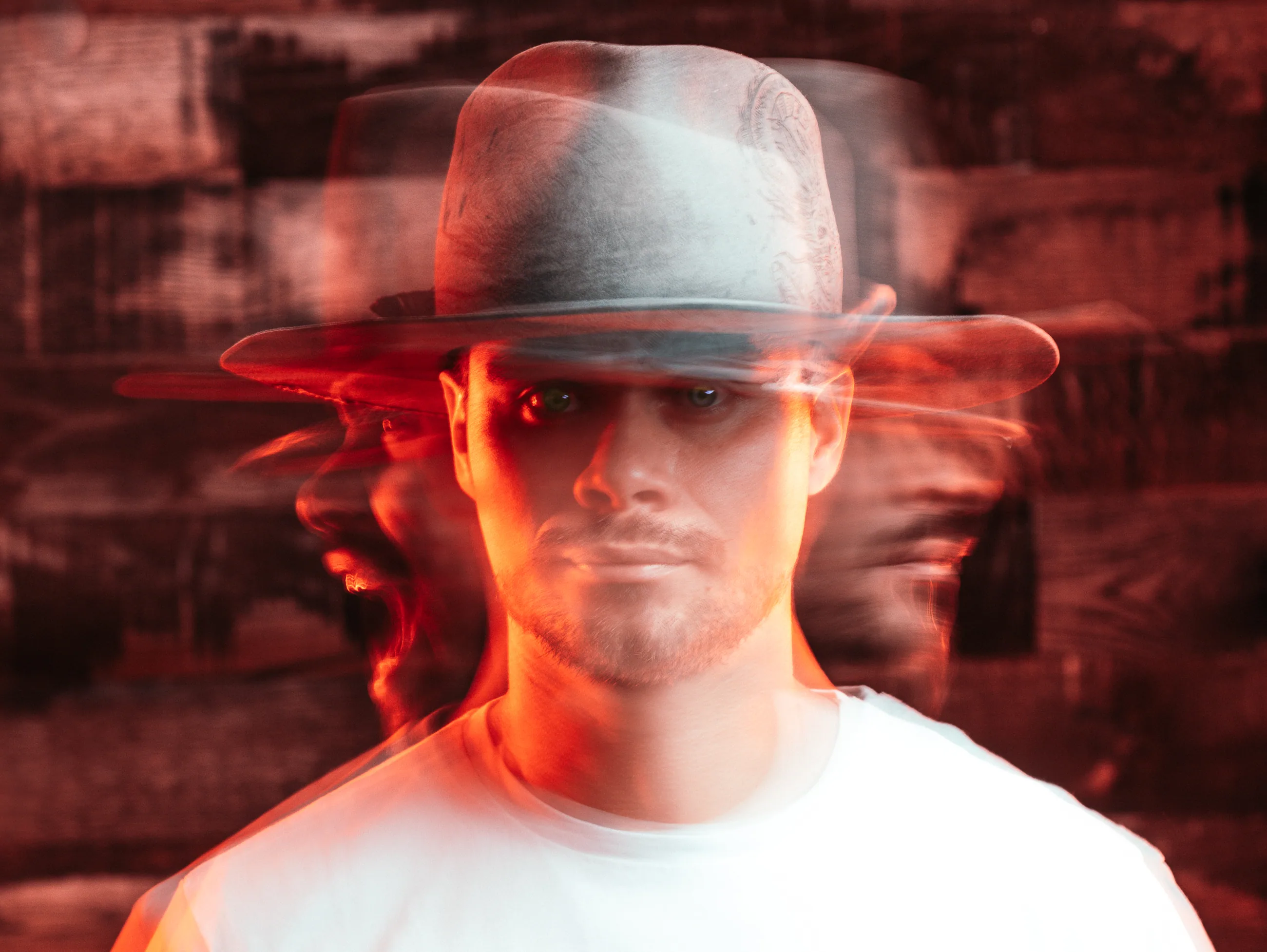 Autorretrato de Elvis Higuera en doble exposición, con sombrero y luz roja